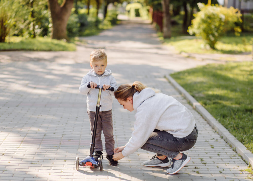 a boy with his mother riding in the park on a scooter